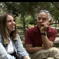 Freed hostages Doron Katz-Asher, left, sits near the grave of her mother Efrat Katz, alongside Efrat's partner, former hostage Gadi Mozes, in Kibbutz Revadim, during an interview broadcast by Channel 12 on May 23, 2025. (Screen capture: Channel 12)